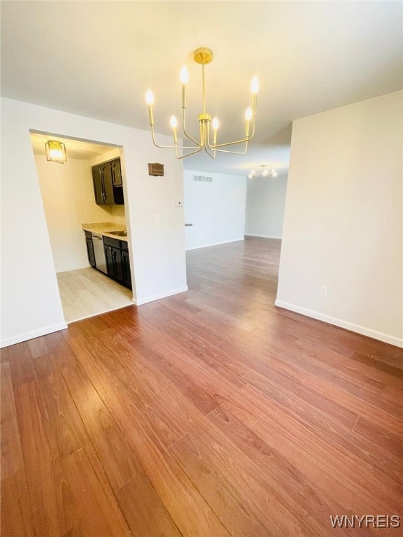 spare room featuring light wood-style floors, baseboards, visible vents, and an inviting chandelier