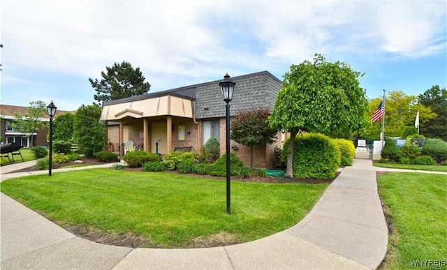 view of front of house with roof with shingles, brick siding, a front lawn, and mansard roof