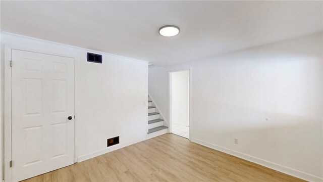 spare room featuring stairs, light wood finished floors, and baseboards