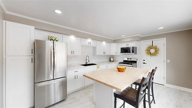 kitchen featuring a sink, white cabinetry, appliances with stainless steel finishes, a kitchen bar, and crown molding