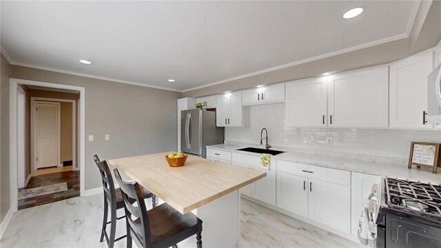 kitchen featuring marble finish floor, gas range oven, ornamental molding, freestanding refrigerator, and a sink