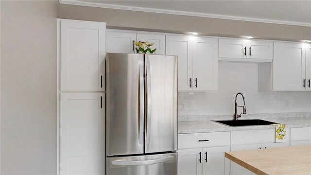 kitchen featuring light countertops, a sink, freestanding refrigerator, and white cabinetry