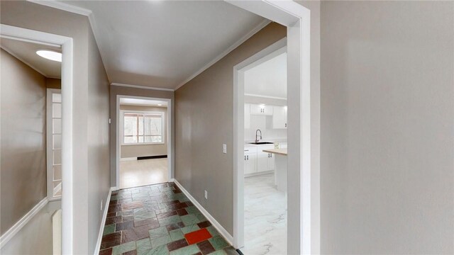 corridor with stone tile flooring, baseboards, ornamental molding, and a sink