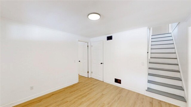 unfurnished room with baseboards, stairway, visible vents, and light wood-style floors