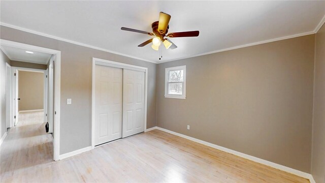 unfurnished bedroom featuring baseboards, a ceiling fan, crown molding, light wood-type flooring, and a closet