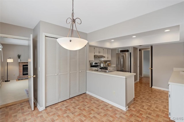 kitchen featuring freestanding refrigerator, a peninsula, light countertops, a sink, and recessed lighting