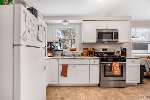 kitchen featuring appliances with stainless steel finishes, a sink, light stone counters, and white cabinets