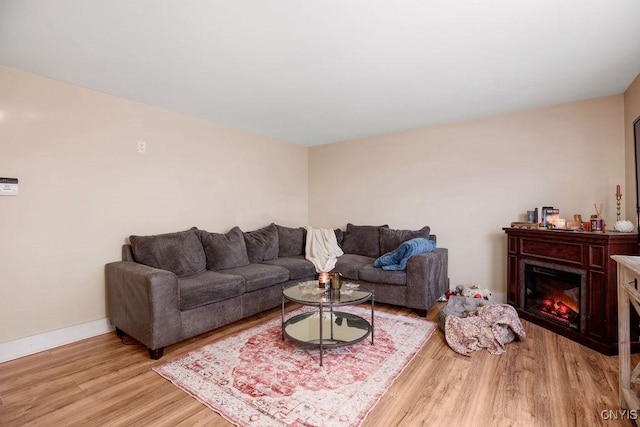 living room featuring light wood-type flooring, a glass covered fireplace, and baseboards