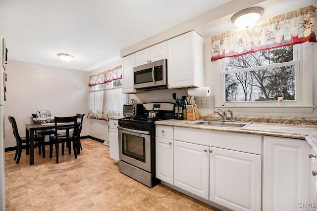 kitchen featuring stainless steel appliances, white cabinets, a sink, and baseboards