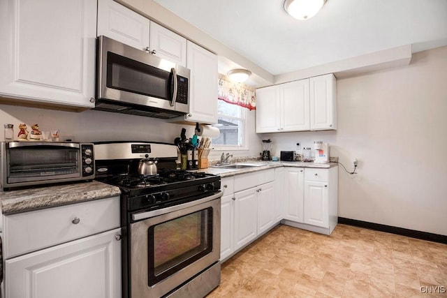 kitchen with baseboards, appliances with stainless steel finishes, a sink, and white cabinets