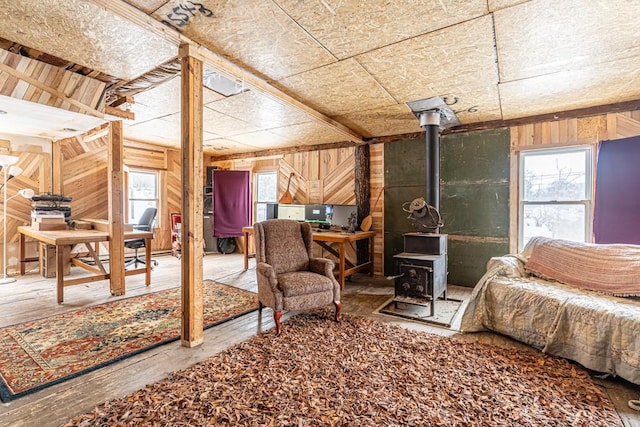 bedroom with a wood stove, multiple windows, wood walls, and hardwood / wood-style flooring