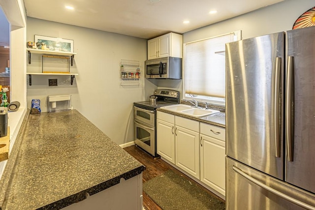 kitchen featuring dark wood finished floors, stainless steel appliances, dark countertops, white cabinetry, and a sink