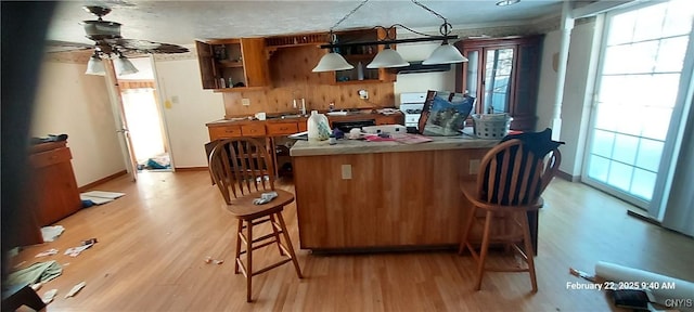 kitchen featuring a ceiling fan, a kitchen breakfast bar, brown cabinets, open shelves, and light wood finished floors