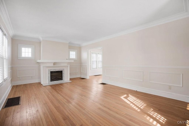 unfurnished living room with light wood finished floors, a premium fireplace, visible vents, and crown molding