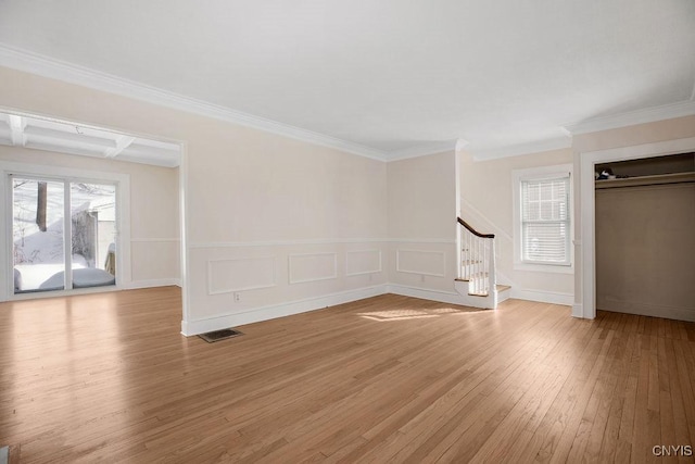 unfurnished living room with a wainscoted wall, visible vents, ornamental molding, stairway, and light wood-type flooring