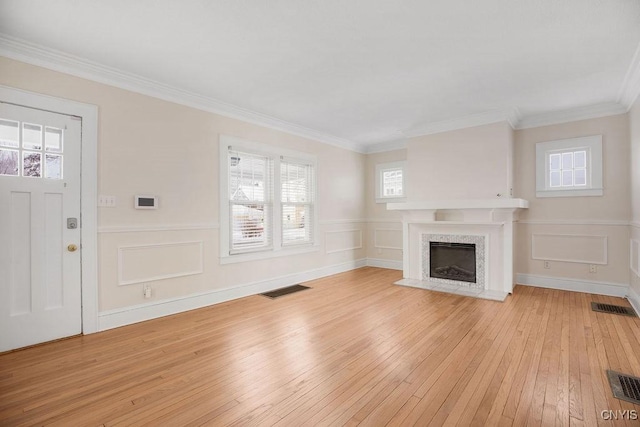 unfurnished living room with light wood-type flooring, visible vents, crown molding, and a high end fireplace