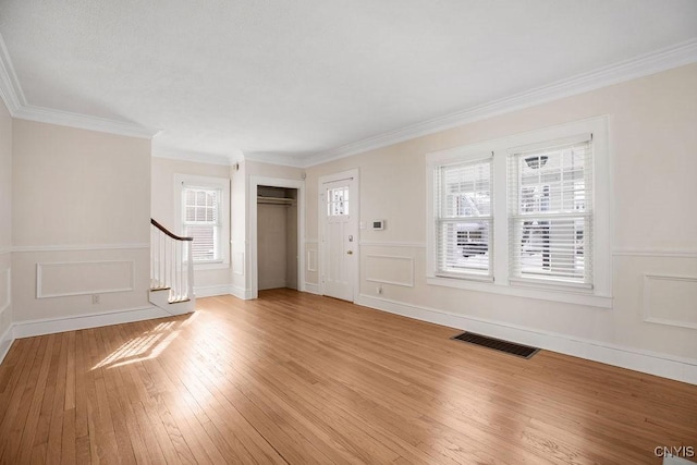 unfurnished living room featuring a decorative wall, visible vents, light wood-style floors, ornamental molding, and stairway