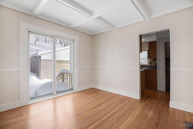 empty room featuring coffered ceiling, baseboards, a healthy amount of sunlight, and light wood finished floors