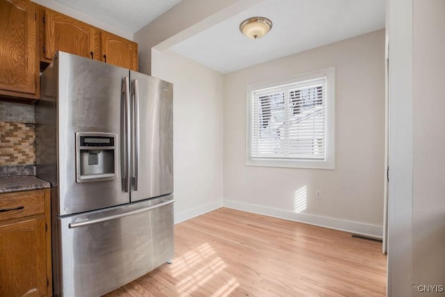 kitchen with brown cabinets, stainless steel fridge, light wood finished floors, and tasteful backsplash