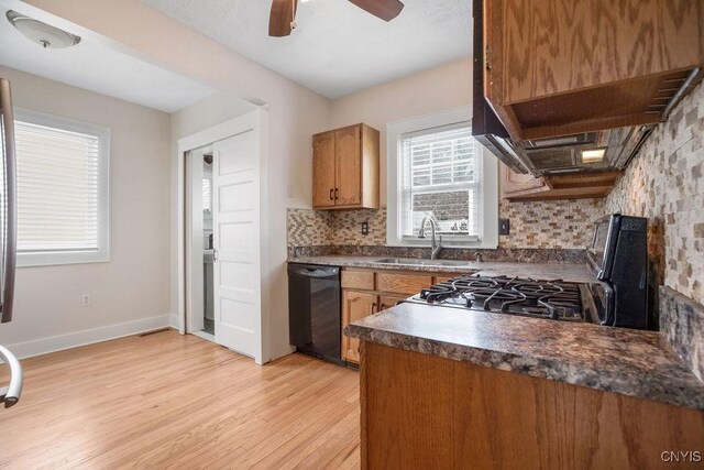 kitchen featuring black dishwasher, dark countertops, light wood-style flooring, a sink, and backsplash