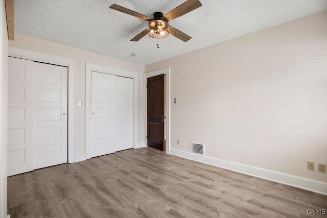 unfurnished bedroom with baseboards, visible vents, ceiling fan, wood finished floors, and a textured ceiling