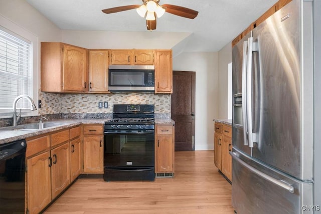 kitchen featuring a sink, black appliances, light wood finished floors, and backsplash