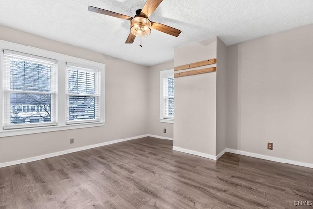 empty room featuring a healthy amount of sunlight, a textured ceiling, baseboards, and wood finished floors