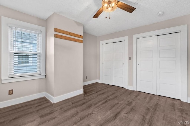 unfurnished bedroom with wood finished floors, two closets, and baseboards