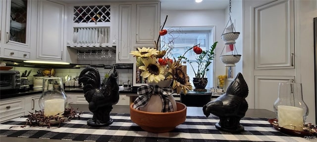 interior space with tasteful backsplash, glass insert cabinets, dark countertops, and white cabinetry