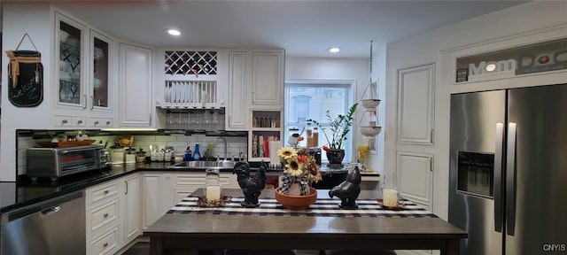 kitchen with dark countertops, backsplash, appliances with stainless steel finishes, white cabinetry, and a sink