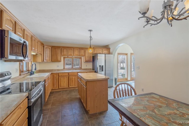 kitchen featuring arched walkways, a kitchen island, stainless steel appliances, light countertops, and a sink