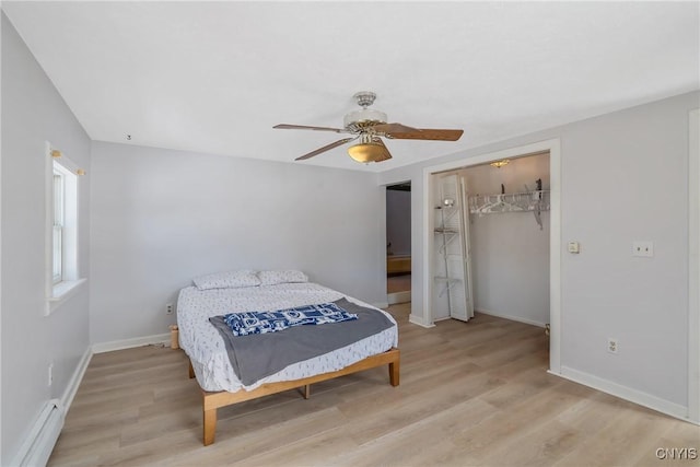 bedroom with baseboard heating, a closet, baseboards, and light wood finished floors