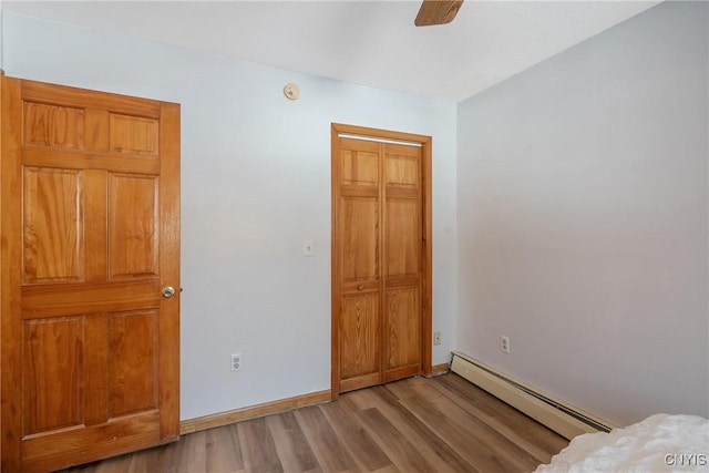 unfurnished bedroom featuring light wood finished floors, baseboards, a baseboard heating unit, and a closet