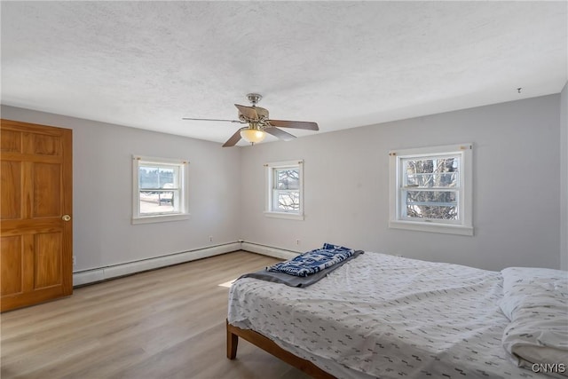 bedroom with a baseboard heating unit, light wood-type flooring, multiple windows, and a textured ceiling