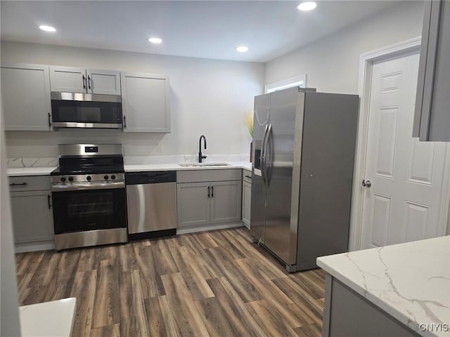 kitchen with dark wood-style floors, light stone countertops, stainless steel appliances, gray cabinetry, and a sink