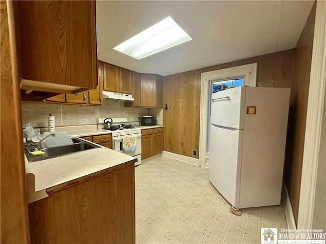 kitchen featuring light floors, brown cabinetry, a sink, white appliances, and under cabinet range hood