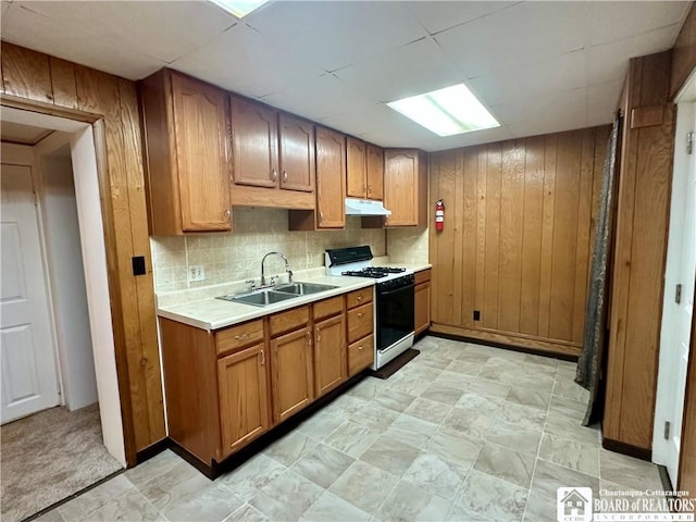 kitchen featuring light countertops, wood walls, gas stove, and a sink