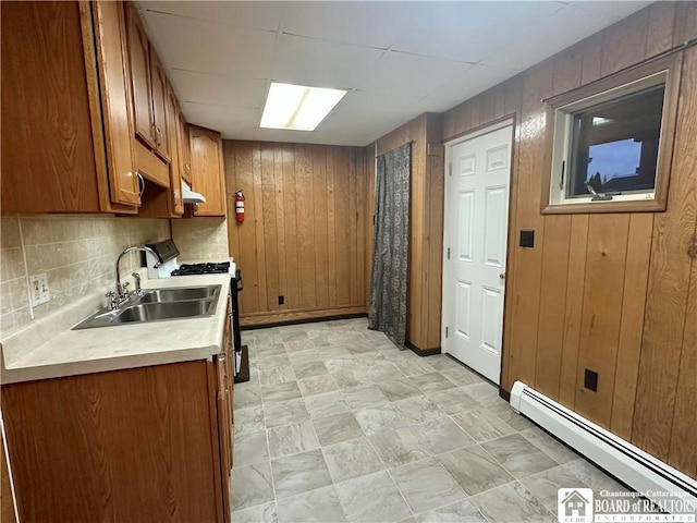 kitchen featuring brown cabinets, gas range oven, light countertops, baseboard heating, and a sink