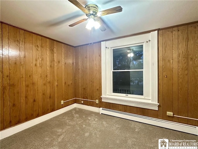 spare room featuring carpet, a baseboard radiator, and wood walls