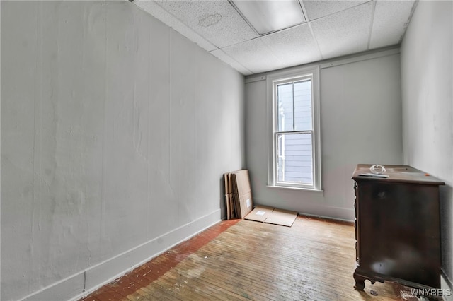 empty room featuring a paneled ceiling, baseboards, and hardwood / wood-style flooring