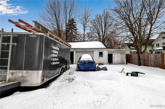 view of snowy exterior with a garage, an outdoor structure, and fence