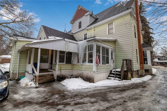 snow covered house featuring a shingled roof and covered porch