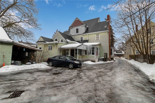 snow covered back of property featuring a chimney and roof with shingles