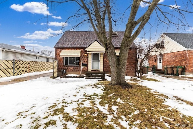 bungalow with brick siding, a shingled roof, and fence