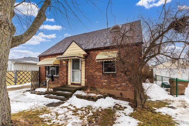 view of front of property featuring a shingled roof, brick siding, and fence