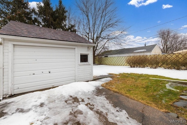 snow covered garage featuring fence, a detached garage, and a lawn