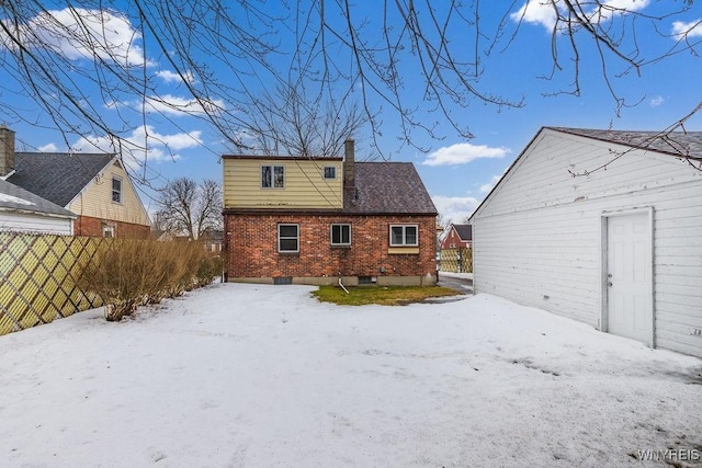 snow covered rear of property featuring brick siding, fence, a chimney, and an outdoor structure