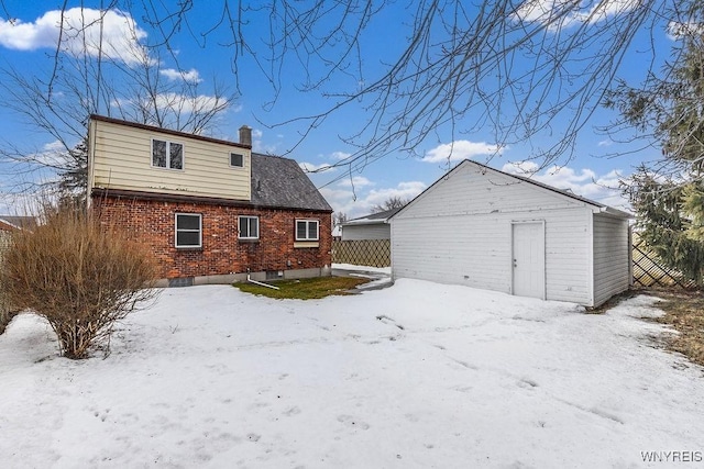 snow covered house with a chimney, fence, an outbuilding, and brick siding