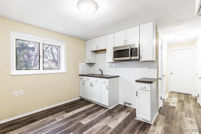 kitchen featuring dark countertops, dark wood finished floors, stainless steel microwave, and a sink