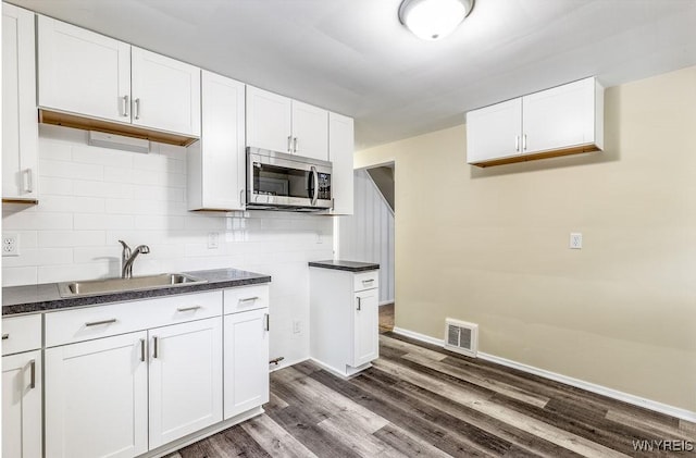 kitchen with visible vents, dark countertops, dark wood-style floors, stainless steel microwave, and a sink